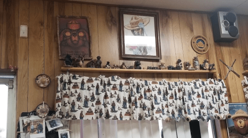 A wooden wall with framed art, a shelf of figurines, and a patterned curtain in a cozy room.